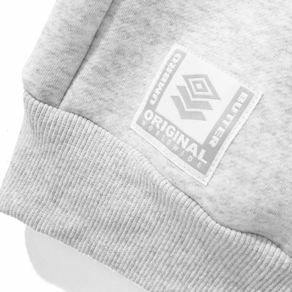 Close-up of the BUTTER GOODS X UMBRO DIAMOND LOGO CREWNECK ASH, featuring a gray cotton blend with a patch displaying "Butter Original Worldwide" and an embroidered geometric logo.