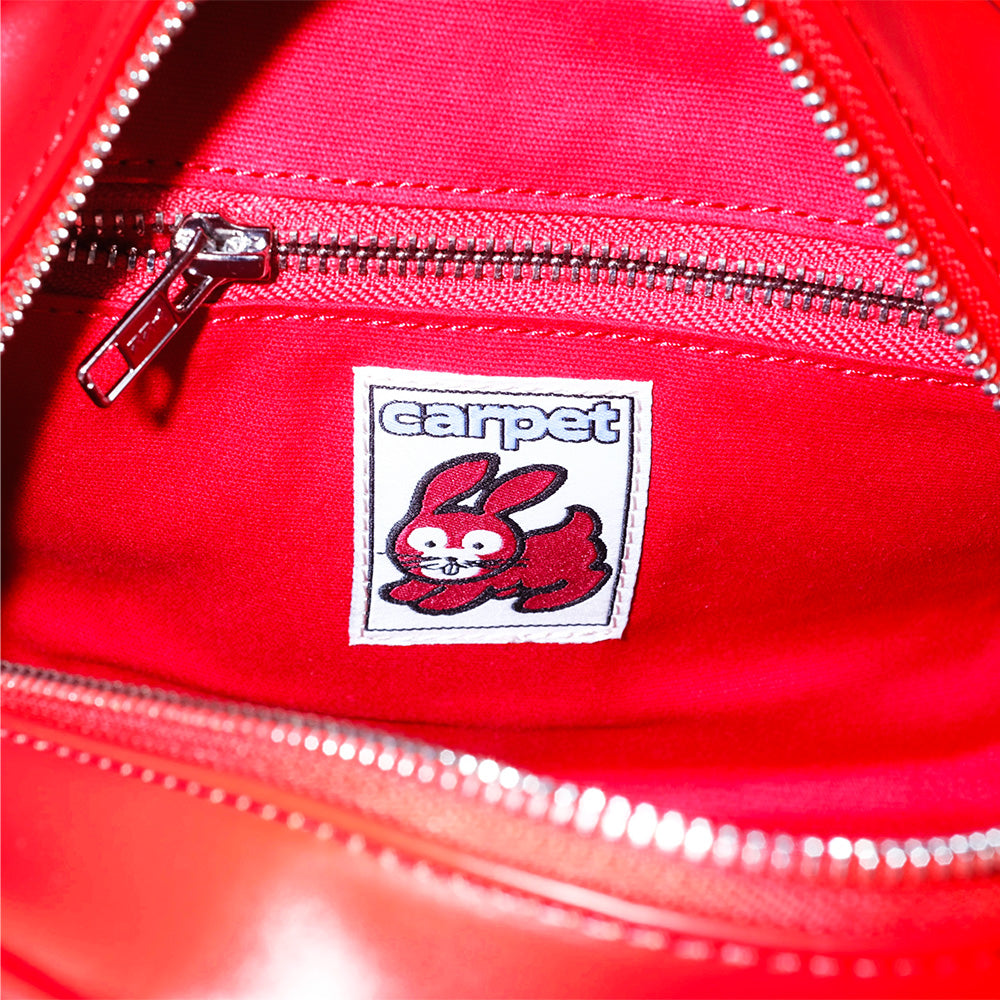 Close-up of the Carpet Co. C-Star Purse Red interior, featuring a zippered pocket and a sewn patch with a cartoon rabbit, the word "carpet," and playful carpet-themed embellishments.