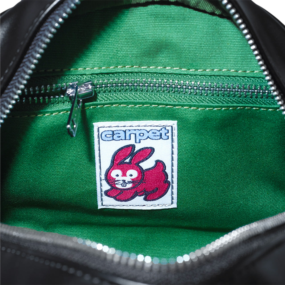 The CARPET CO. C-STAR PURSE BLACK by Bluetile Skateboards features a green-lined interior with a zippered pocket and a sewn label showing a red cartoon rabbit and "carpet" in blue, adding playful accents.