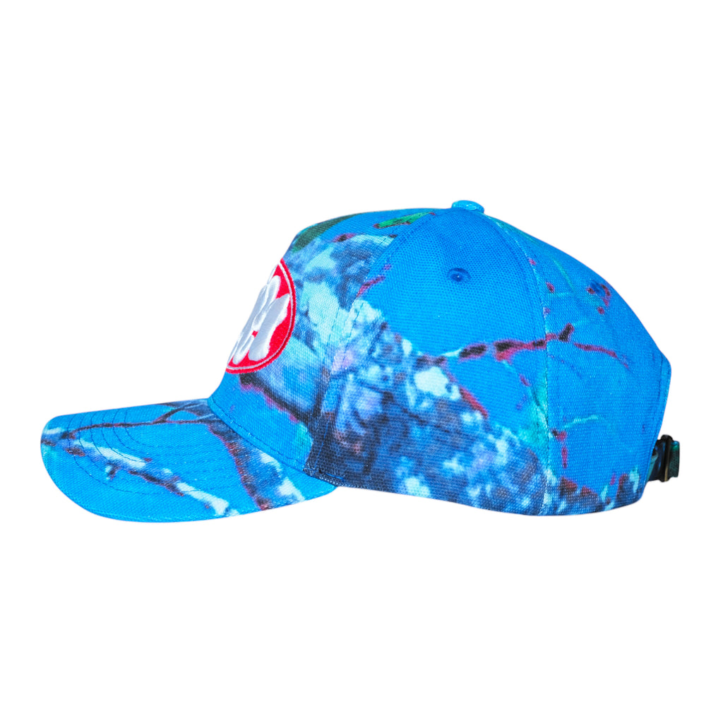 The left profile of the CARPET CO. REALTREE HAT BLUE by Carpet Co. reveals a blue tie-dye baseball cap with an embroidered white "00" inside a red circle, reminiscent of a Realtree pattern.