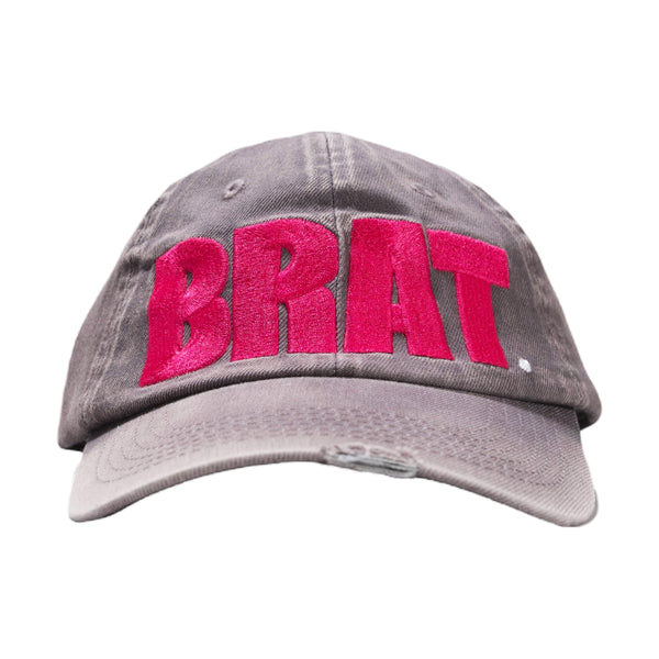 Gray denim baseball cap with the word "brat" embroidered in bold pink letters isolated on a white background by Carpet Co.