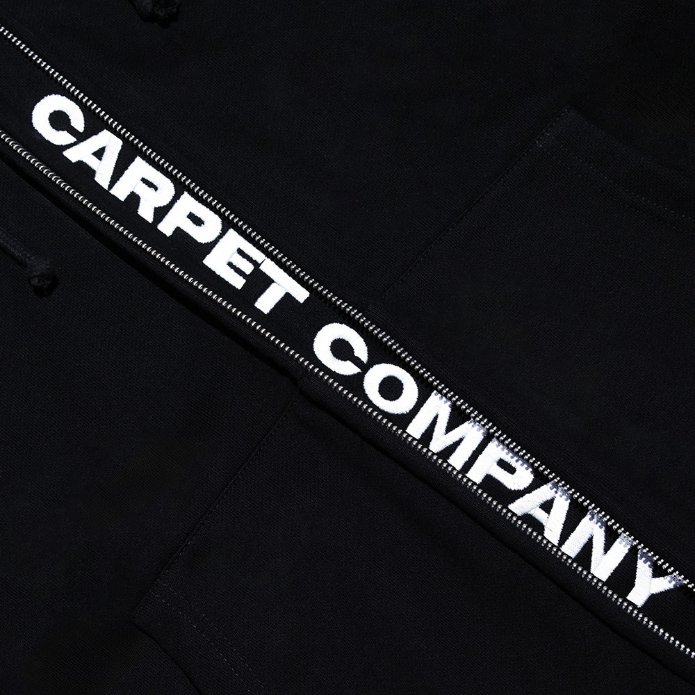 The Carpet Co. FAKE ZIP UP HOODIE BLACK is a black hoodie with double zips and bold white "CARPET COMPANY" text on a stitched strip, giving this standout design a sleek finish.