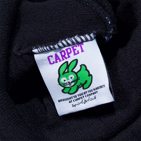 Clothing tag with a green cartoon bunny, "CARPET" in purple, and text in English and Arabic from Carpet Co. Adds the perfect touch to your CARPET CO. FREESTYLE BEANIE BLACK by Carpet Co.