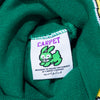 The CARPET CO. FREESTYLE BEANIE GREEN by Carpet Co. has a clothing tag on green fabric with a cartoon rabbit, "CARPET" text, and the note: "Brought to you by the habibis at Carpet Co" in English and Arabic.
