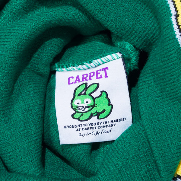 The CARPET CO. FREESTYLE BEANIE GREEN by Carpet Co. has a clothing tag on green fabric with a cartoon rabbit, "CARPET" text, and the note: "Brought to you by the habibis at Carpet Co" in English and Arabic.