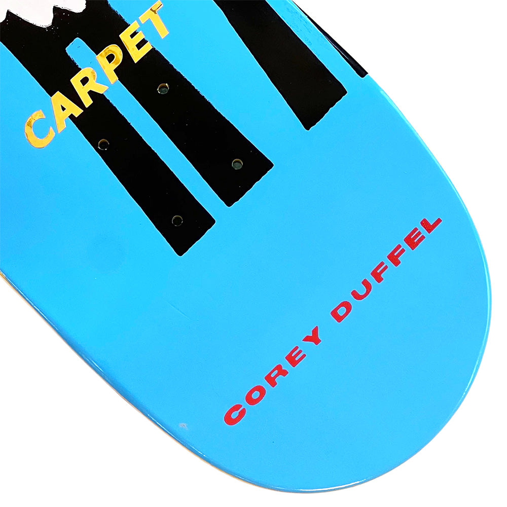 Close-up of the CARPET COREY DUFFEL GUEST DECK by Carpet Co.—a blue limited edition skateboard deck with "CARPET" in yellow and "COREY DUFFEL" in red, celebrating this unique guest release.