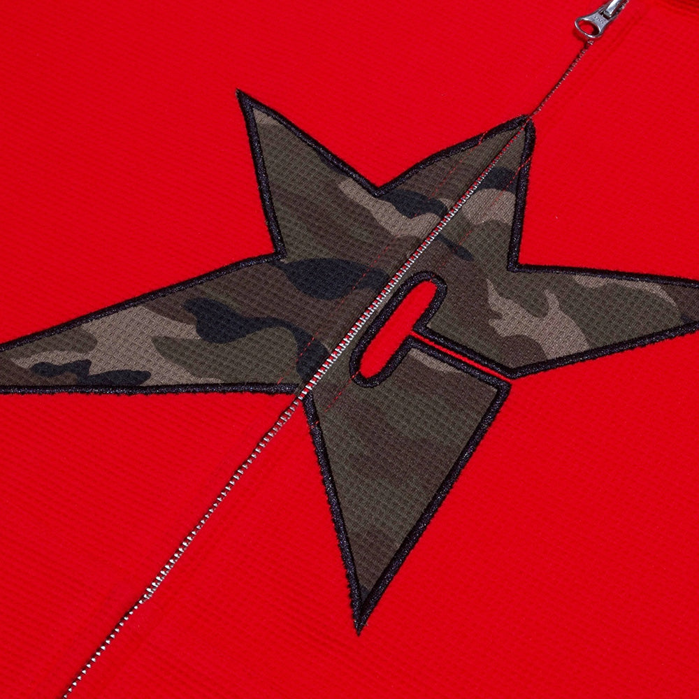 A close-up of the Carpet Co. C-Star Thermal Zip Hoodie Red shows its red fabric, a black-bordered camo star patch, and a visible silver zipper down the center.