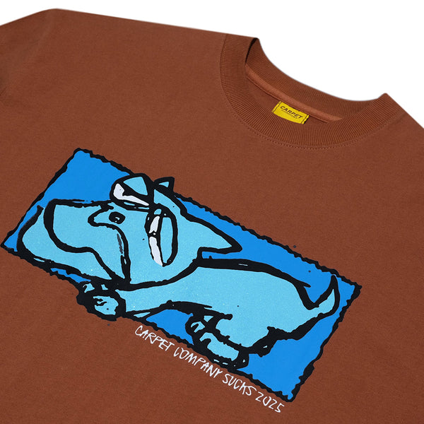 The Carpet Co. Dog Tee Brown features a blue cartoon dog graphic and "CAREY COMPANY SUCKS 2025" text below, offering a unique look inspired by classic print shop rag tees.