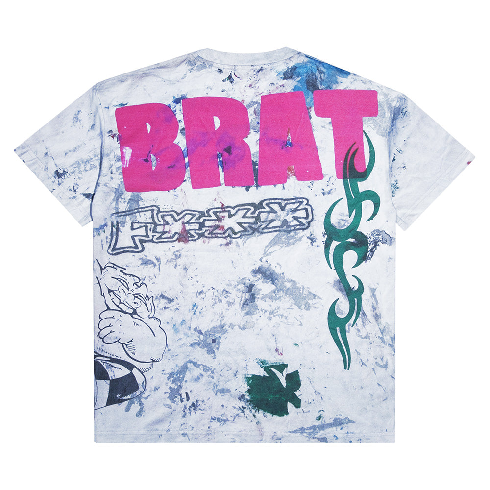 The CARPET CO. RAG TEE by Carpet Co. features blue and purple tie-dye, bold pink “BRAT” graffiti, a tribal design, and a cartoon graphic on the back—style it with black denim for standout streetwear flair.