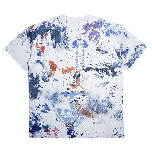 The CARPET CO. RAG TEE by Carpet Co. features a white base with multicolored paint splatters, abstract designs, and "LOVE" in bold on the lower back—pair it with black denim for an artistic statement look.