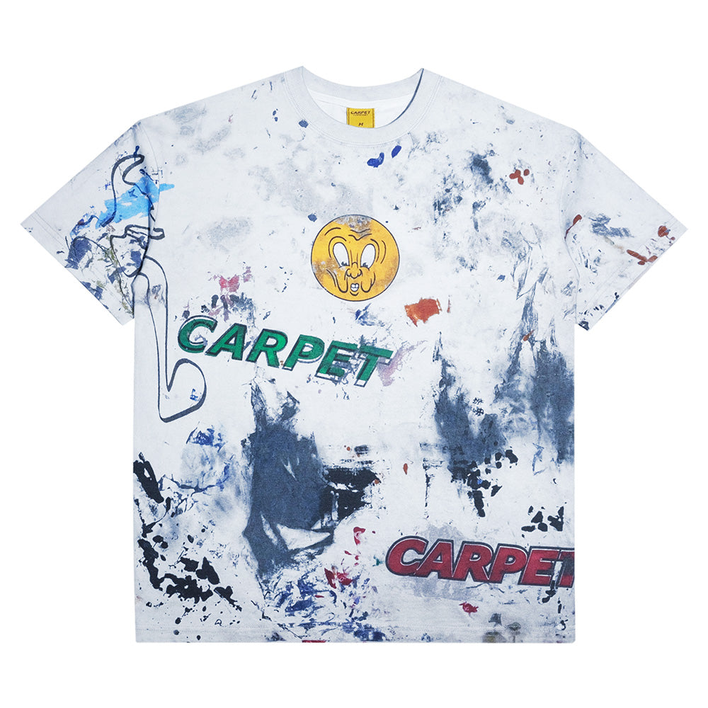 The CARPET CO. RAG TEE by Carpet Co. features abstract paint splatters, double "CARPET" prints, a cartoon face, blue left-side line art, and bold details—ideal to style with black denim for a standout look.