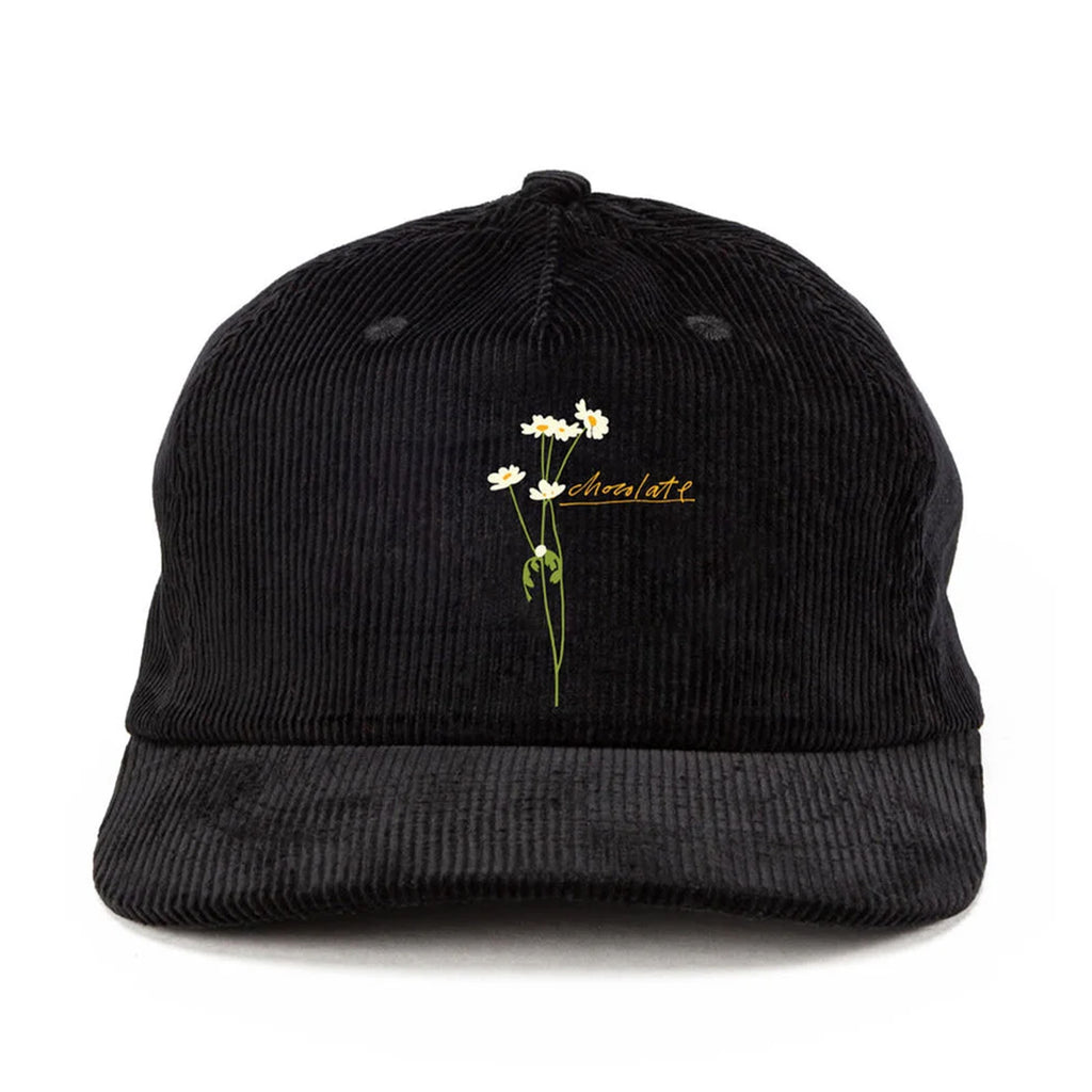 The CHOCOLATE X HECOX STEMS CORD HAT BLACK by CRAILTAP boasts a chic design with an embroidered white daisy and yellow text on black corduroy. This stylish snapback hat offers adjustable fitting for all-day comfort and playful charm.