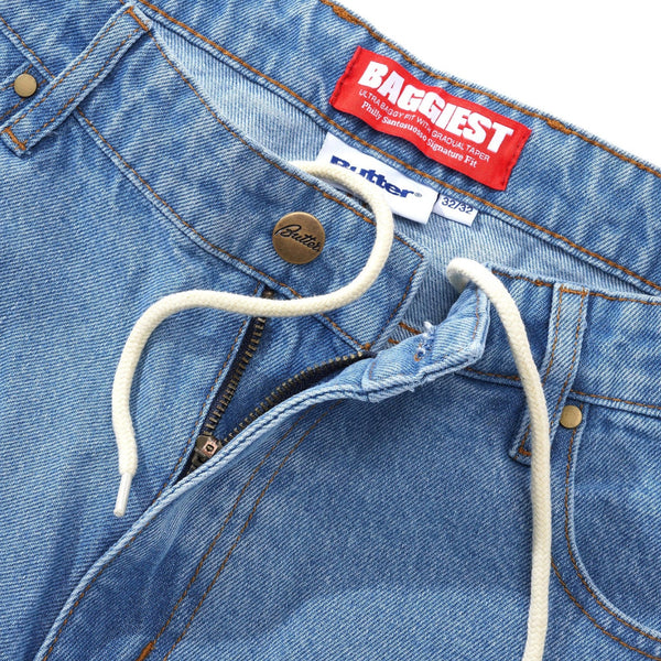 Washed indigo denim pants with a drawstring and zipper closure from Butter Goods. They feature a red "Baggiest" label and another highlighting the comfortable fit, branded as "Butter.