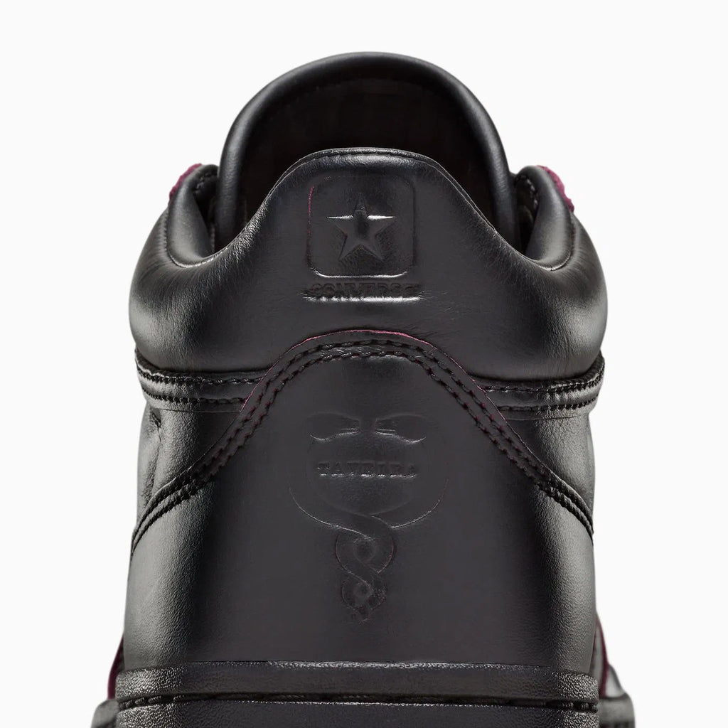 A detailed view of the CONVERSE CONS REMY TAVEIRA FASTBREAK PRO MID in black, showcasing a star emblem and a snake design on the heel, enhanced by a sleek nubuck upper for a sophisticated look.