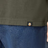 Close-up of a person wearing an olive green DICKIES X SPITFIRE long sleeve tee with a small logo near the hem and blue jeans. A hand is partially visible on the right side.