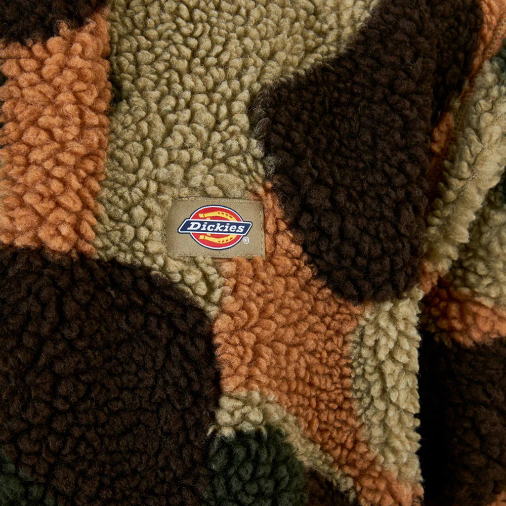 Close-up of a textured fabric pattern in brown, green, and tan patches featuring the DICKIES logo, highlighting the DICKIES Relaxed Fit High Pile Camo Fleece in Imperial Green for ultimate comfort.