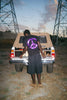 A man wearing a 100% Cotton VIOLET PEACE TEE BLACK from the brand violet stands in the back of a truck, which features reflective vinyl print.