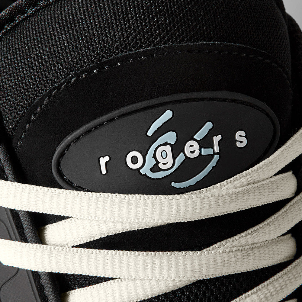 Close-up of the éS TJ ROGERS skate shoe in black, blue, and white by ES, featuring white laces, cupsole construction, and a "rogers" label with a light blue graphic.