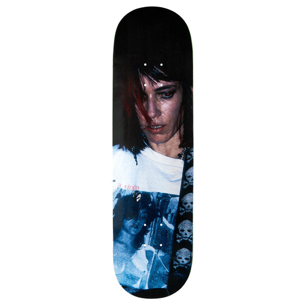A violet skateboard deck featuring a graphic of Kim Gordon with dark hair and a pensive expression, wearing a t-shirt with skull designs and text.