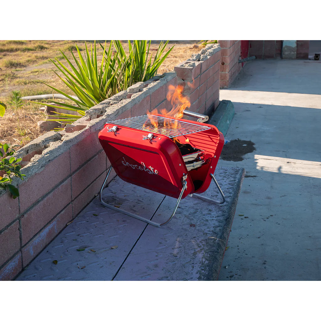 A red CHOCOLATE spot grill sitting on top of a brick wall.