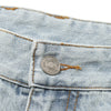 Close-up of the waist area of a pair of HELAS DIEU GREC JEAN SHORT LIGHT BLUE showing a metal button with engraved text, visible yellow stitching, and an embroidered HELAS logo for added detail.