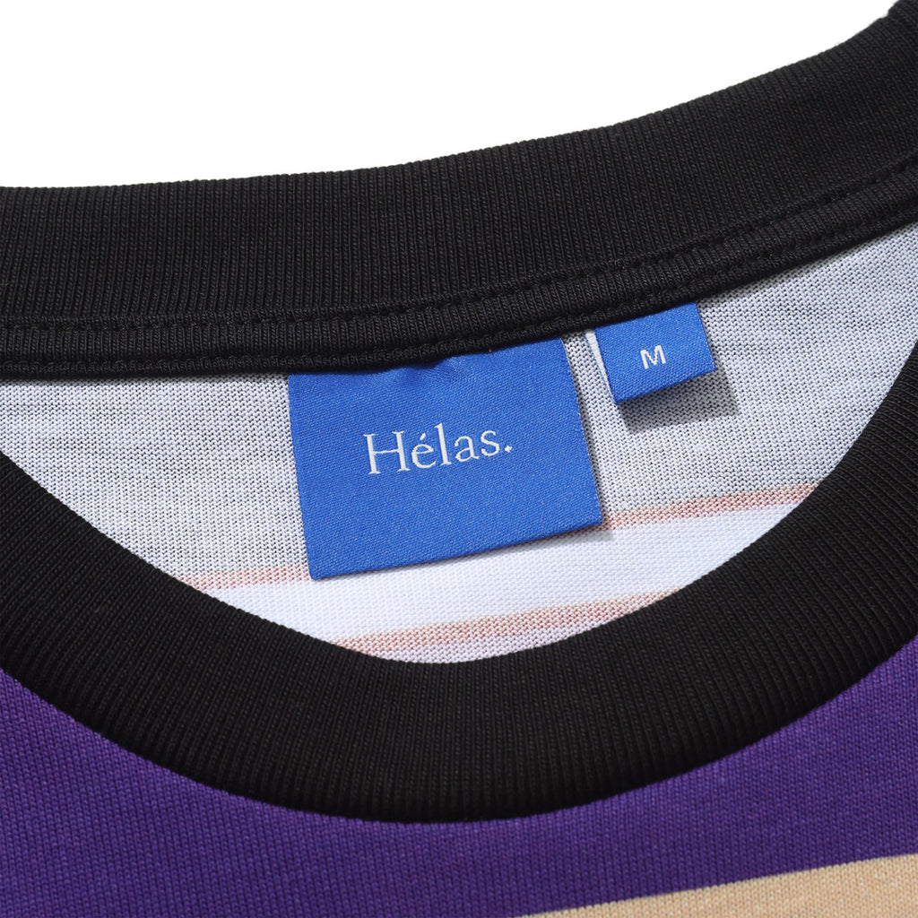 Close-up of a blue "HELAS" clothing tag on a striped HELAS RAYURES TEE PURPLE / BLACK with a black collar, indicating the size "M," and featuring an embroidered umbrella logo.