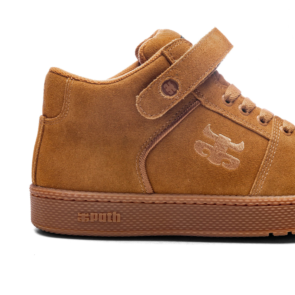 The IPATH GRASSHOPPER COGNAC SUEDE is a high-top sneaker in cognac suede, featuring a Velcro strap, laces, and a stitched emblem on the side. It offers an Ortholite insole for added comfort and boasts a textured rubber sole with the IPATH brand name embossed on it.