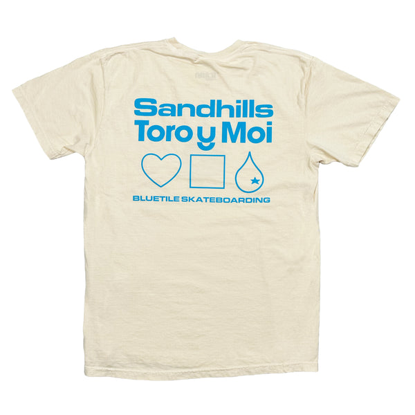An ivory tee with blue words that say "Sandhills, Toro Y Moi, Bluetile Skateboarding" and a heart, square, and water drop.