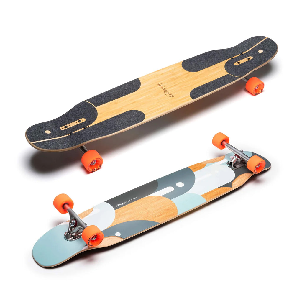 Two longboards are shown. The Loaded Mata Hari 44.5" Complete features a wooden top with black grip tape and orange wheels, perfect for urban exploration. The other displays a colorful graphic design on the underside with light blue and orange hues, complemented by its striking orange wheels.
