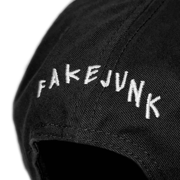 Close-up of black fabric with white embroidered text that reads "FAKE JUNK" on the FAKE JUNK LOGO DAD HAT BLACK from the FAKE JUNK brand, made of 100% cotton.