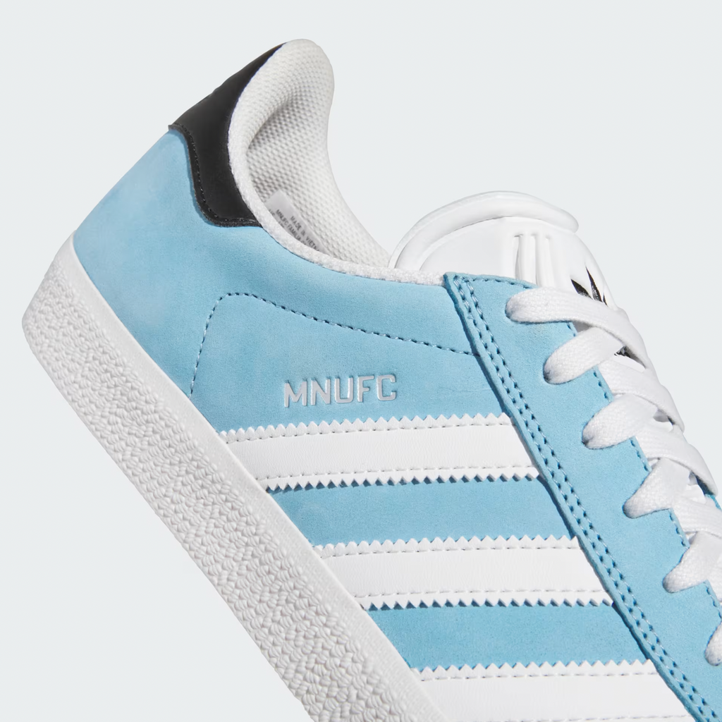 A close-up of the ADIDAS X MNUFC X FAMILIA GAZELLE ADV CRYSTAL WHITE / CORE BLACK / BETTER SCARLET showcases its premium suede upper, emphasizing the flexible cupsole construction that guarantees both style and comfort.