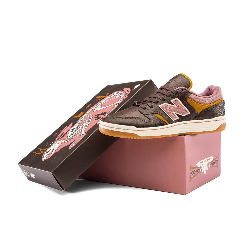 A pair of brown NB NUMERIC sneakers with pink accents, featuring an ABZORB in-sole, next to an open shoebox with a dragon design.