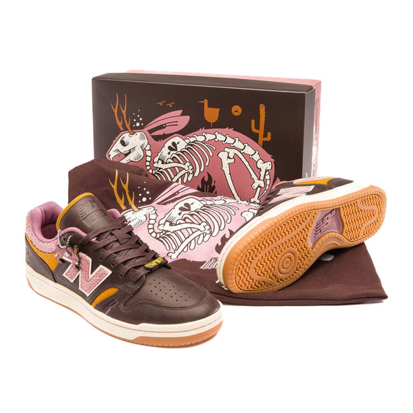 A pair of NB NUMERIC sneakers featuring ABZORB in-sole technology with a color palette of pink, purple, and brown, displayed alongside a matching illustrated shoebox, all set against a white background.
