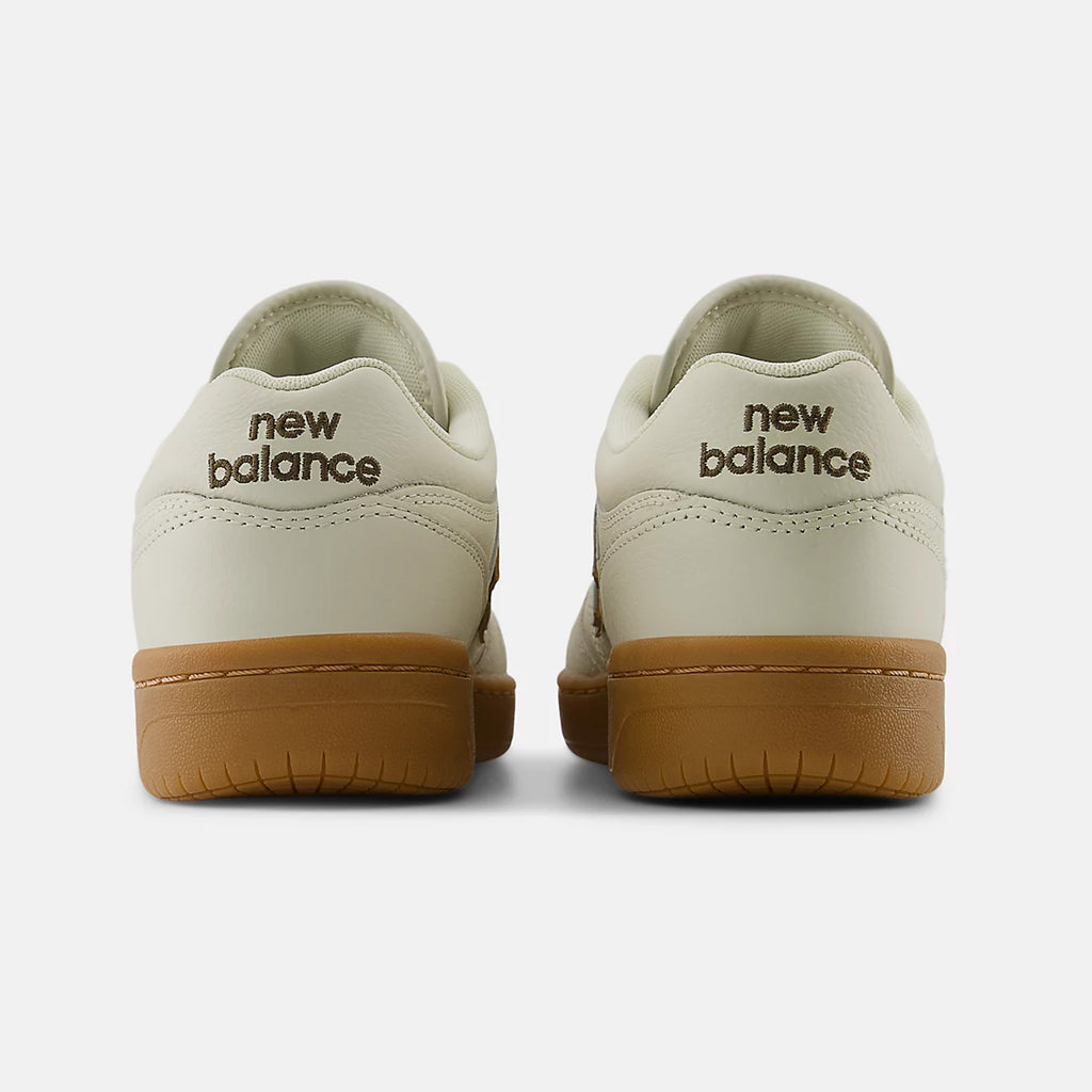 Rear view of a pair of NB Numeric Andrew Reynolds 480 sneakers in sea salt and brown, featuring the brand name "NB Numeric" in brown text on the heels. These shoes also incorporate FuelCell foam technology for enhanced comfort and responsiveness.