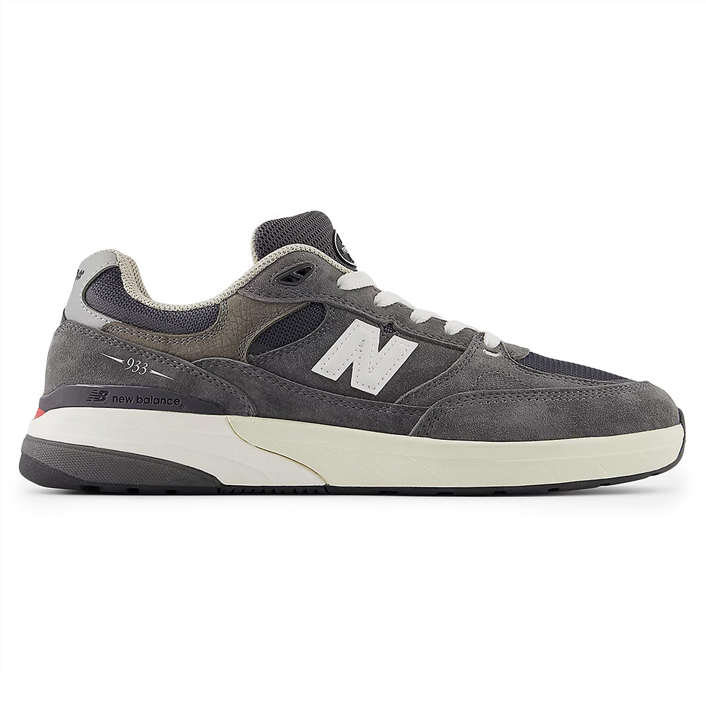The NB NUMERIC "GREY DAYS" REYNOLDS 933 in dark grey and white features a cream sole, white laces, and a signature "N" logo. Premium cushioning enhances comfort. Shown in profile view against a white background.