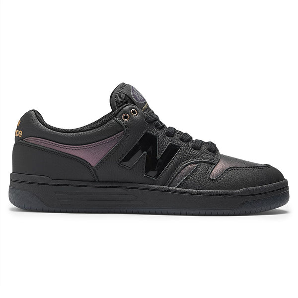 The NB NUMERIC X BRONZE56K 480 is a black low-top sneaker by NB NUMERIC, featuring a glossy black "N" logo, gold accents, a rubber sole with ABZORB cushioning, and shown in side profile.