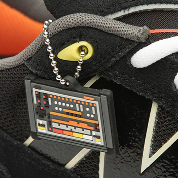 Close-up of the NB Numeric x Roland 808 Tiago sneaker in black and orange, adorned with an orange lining and a small, detailed keychain that resembles a vintage synthesizer attached to the laces.