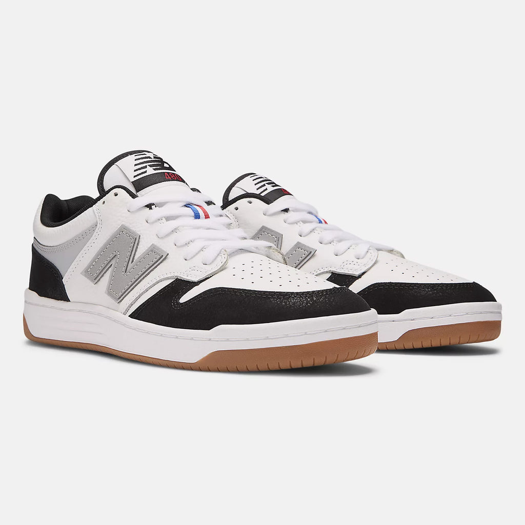 The NB Numeric 480 Tiago x Kawhi sneakers from NB Numeric are a stylish pair of white, black, and grey heritage hightop basketball shoes with gum soles. They feature the New Balance logo on the sides and red-blue accents on the laces, and are equipped with FuelCell foam for exceptional comfort.