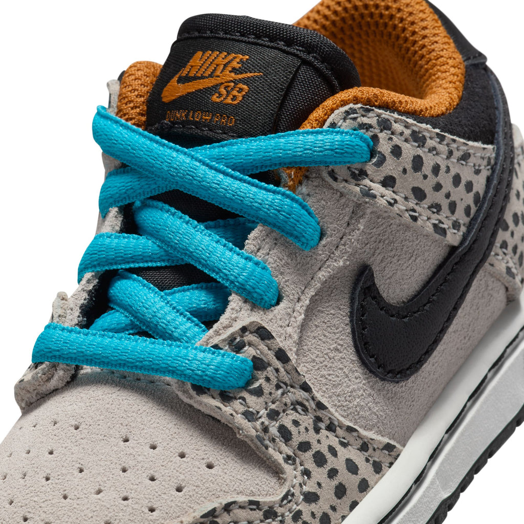 Close-up of the NIKE SB DUNK LOW PRO ELECTRIC TD PHANTOM/BLACK sneaker by Nike, showcasing blue laces, a black swoosh, and a grey and black spotted design with an orange inner lining. Ideal for pairing with skateboards or as stylish toddler shoes.