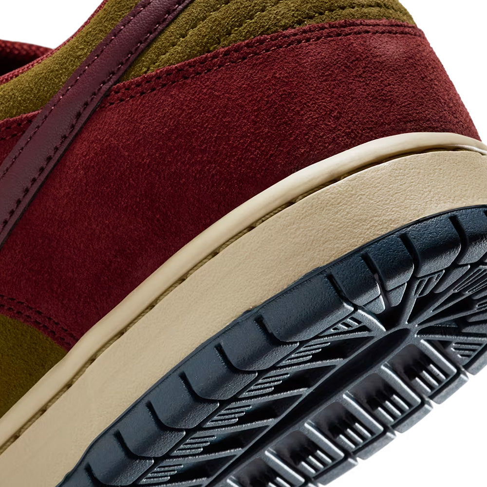 Close-up of the heel and outsole of the NIKE SB DUNK LOW PRO DARK TEAM RED / OLIVE FLAK by nike, showcasing a suede upper in Dark Team Red and Olive Flak with a beige midsole and black textured rubber outsole.