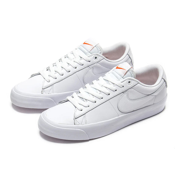 A pair of NIKE SB ORANGE LABEL BLAZER LOW PRO GT ISO shoes in white with white laces, a white sole, and an orange logo on the tongue that are perfect for skateboards. These BLAZER LOW sneakers effortlessly blend classic style with modern functionality.