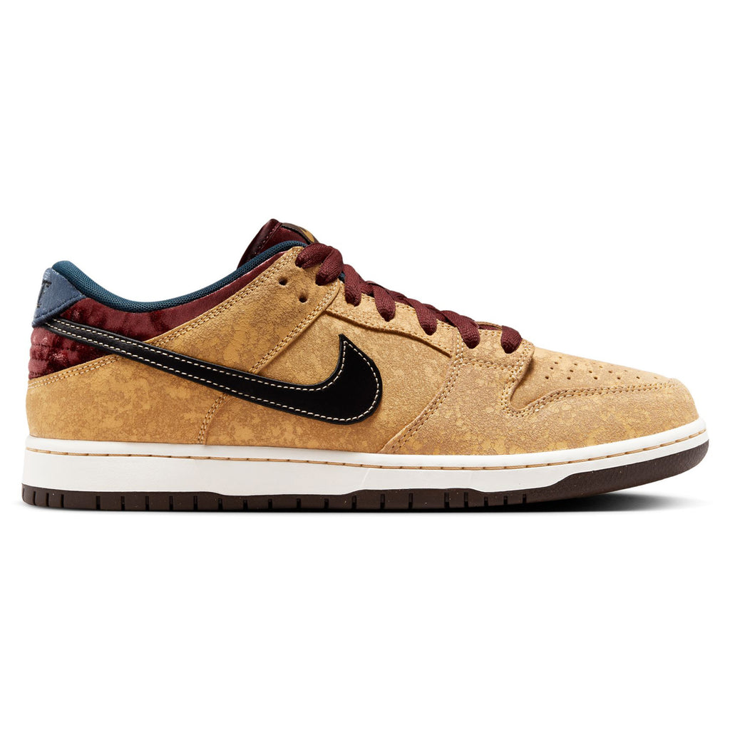 The NIKE SB DUNK LOW PRO CELESTIAL GOLD/BLACK-DARK TEAM RED offers a tan sneaker with a textured suede upper, highlighted by a black swoosh, maroon laces, and an elegant white and brown sole.