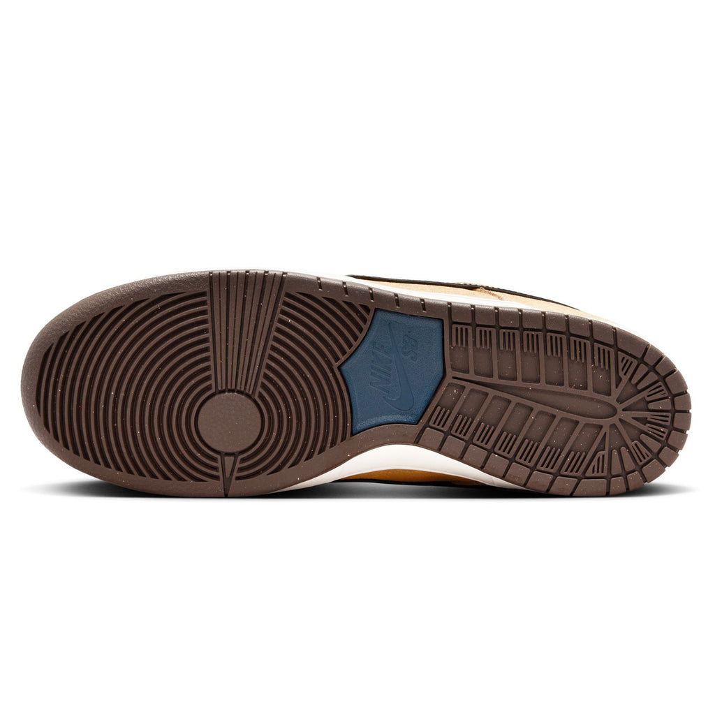 The sole of the NIKE SB DUNK LOW PRO CELESTIAL GOLD/BLACK-DARK TEAM RED showcases a circular tread pattern in a light brown color, highlighted by a striking blue hexagonal detail at the center. The foam midsole ensures cushioned comfort with each step, while the suede upper enhances both elegance and durability.