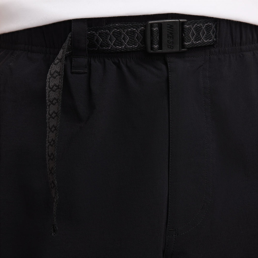 Close-up image of NIKE SB KEARNY CARGO SKATE PANTS BLACK by nike, featuring an elastic waistband, drawstring, and a belt with a decorative pattern. These lightweight, sweat-wicking pants offer a customizable fit perfect for any activity.