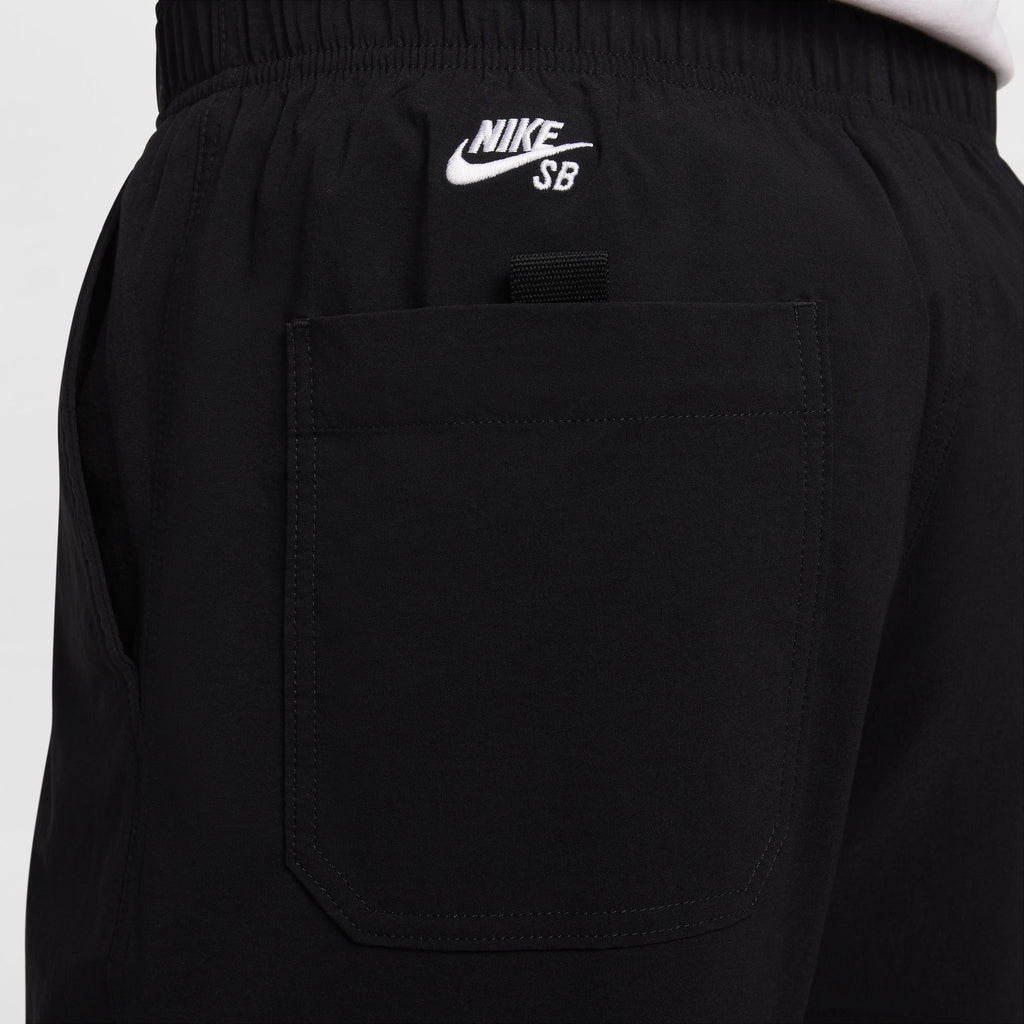 Close-up of the back of a person wearing black NIKE SB KEARNY CARGO SKATE PANTS from Nike, featuring an elastic waistband and a patch pocket on the right side with an embroidered Nike logo above it. These lightweight, sweat-wicking pants offer a customizable fit for maximum comfort.