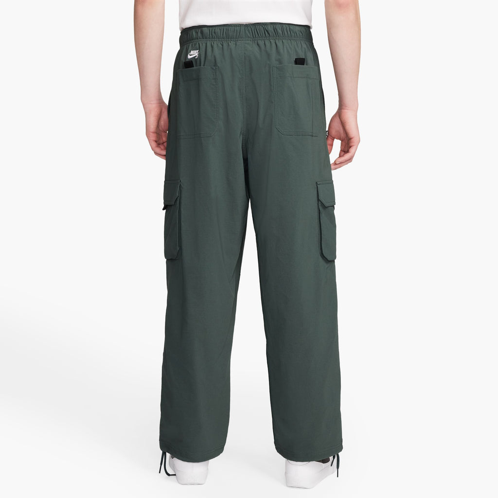 A person wearing NIKE SB KEARNY Cargo Skate Pants in vintage green from nike, viewed from the back, with multiple pockets.