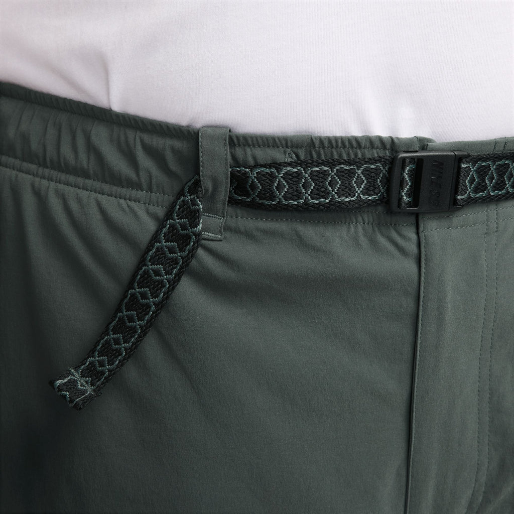 Close-up of a person wearing vintage green, loose-fit NIKE SB KEARNY CARGO SKATE PANTS with a textured belt and a tucked-in white shirt, exuding casual elegance similar to Nike SB Skyring skate shorts.