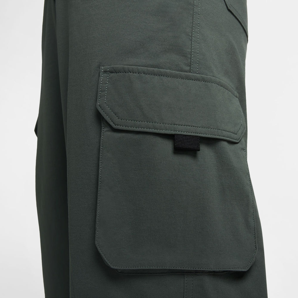 Close-up of a dark green pocket on a pair of NIKE SB Kearny Cargo Skate Pants Vintage Green, showcasing the flap detail with a black strip underneath. The clothing appears to be made of a smooth, durable fabric and offers a loose fit for comfort.