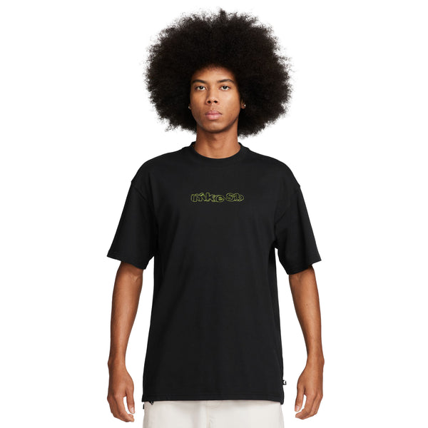 Person standing against a plain background, wearing a black NIKE SB Sounds Bangin Skate Tee with a green "NIKE SB" logo and light-colored pants. The midweight cotton tee complements the individual's afro hairstyle.