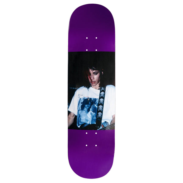 A skateboard deck with a Violet “Ode to Kim” inset purple woodgrain veneer, featuring a central black and white photo of a young man with medium-length hair, wearing a graphic t-shirt.